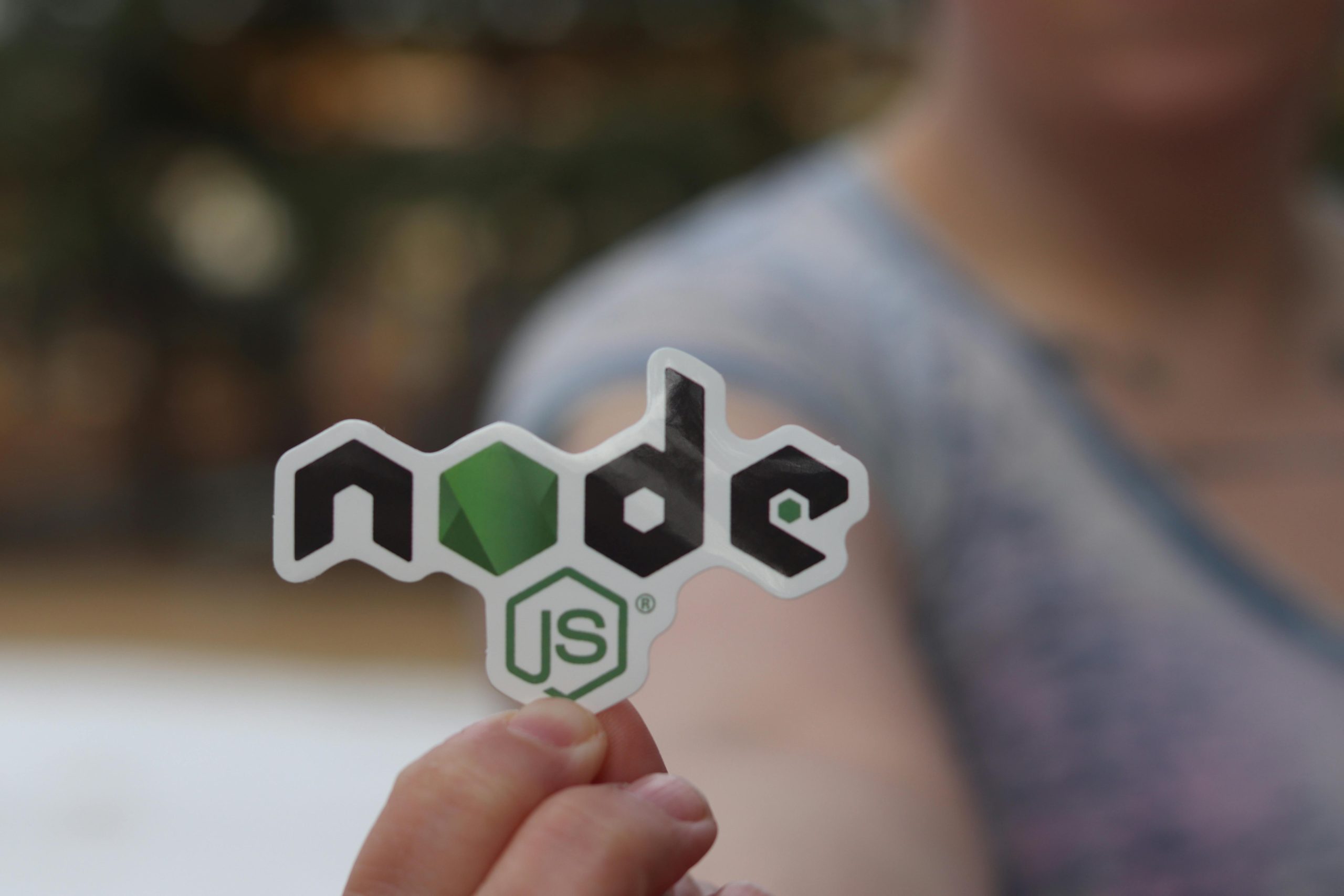 A person holding a Node.js sticker with a blurred background, close-up shot.